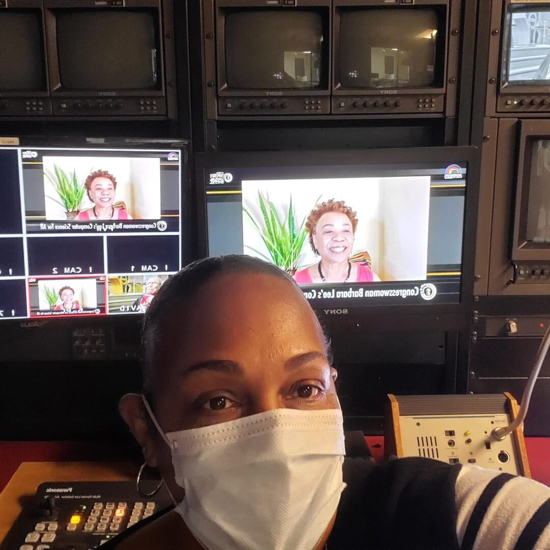 A woman wearing a face mask in front of tv screens.