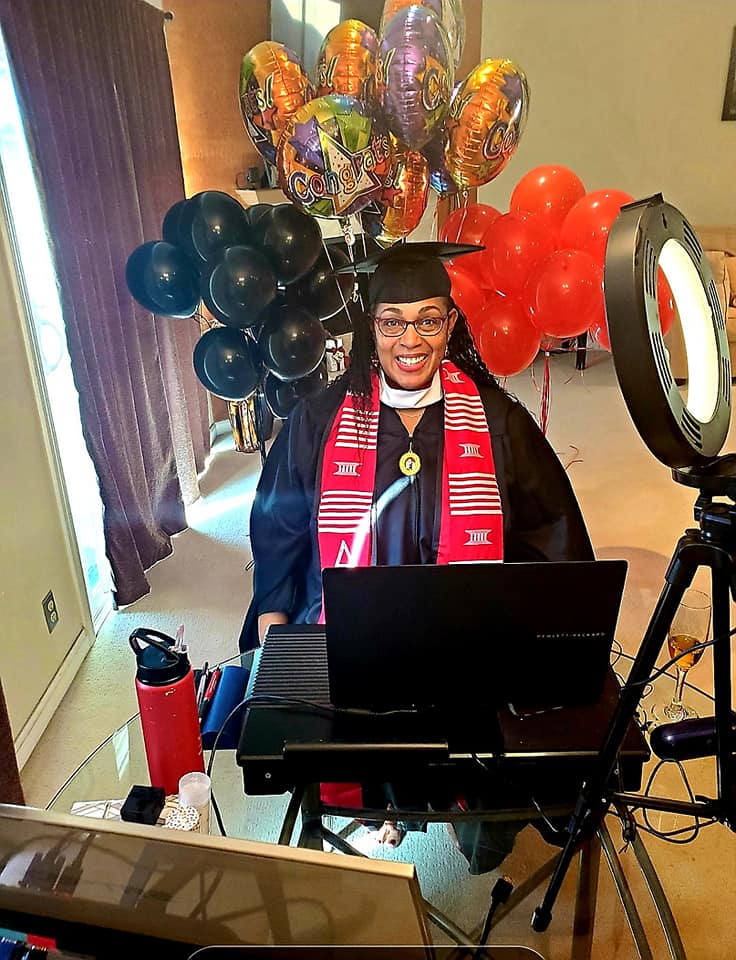 A woman in graduation cap and gown sitting at a laptop.