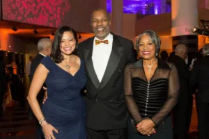 Three smiling adults in formal attire at event